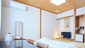 Habitación de hotel con cama, escritorio con silla, televisor, refrigerador pequeño y aire acondicionado instalado en la pared.