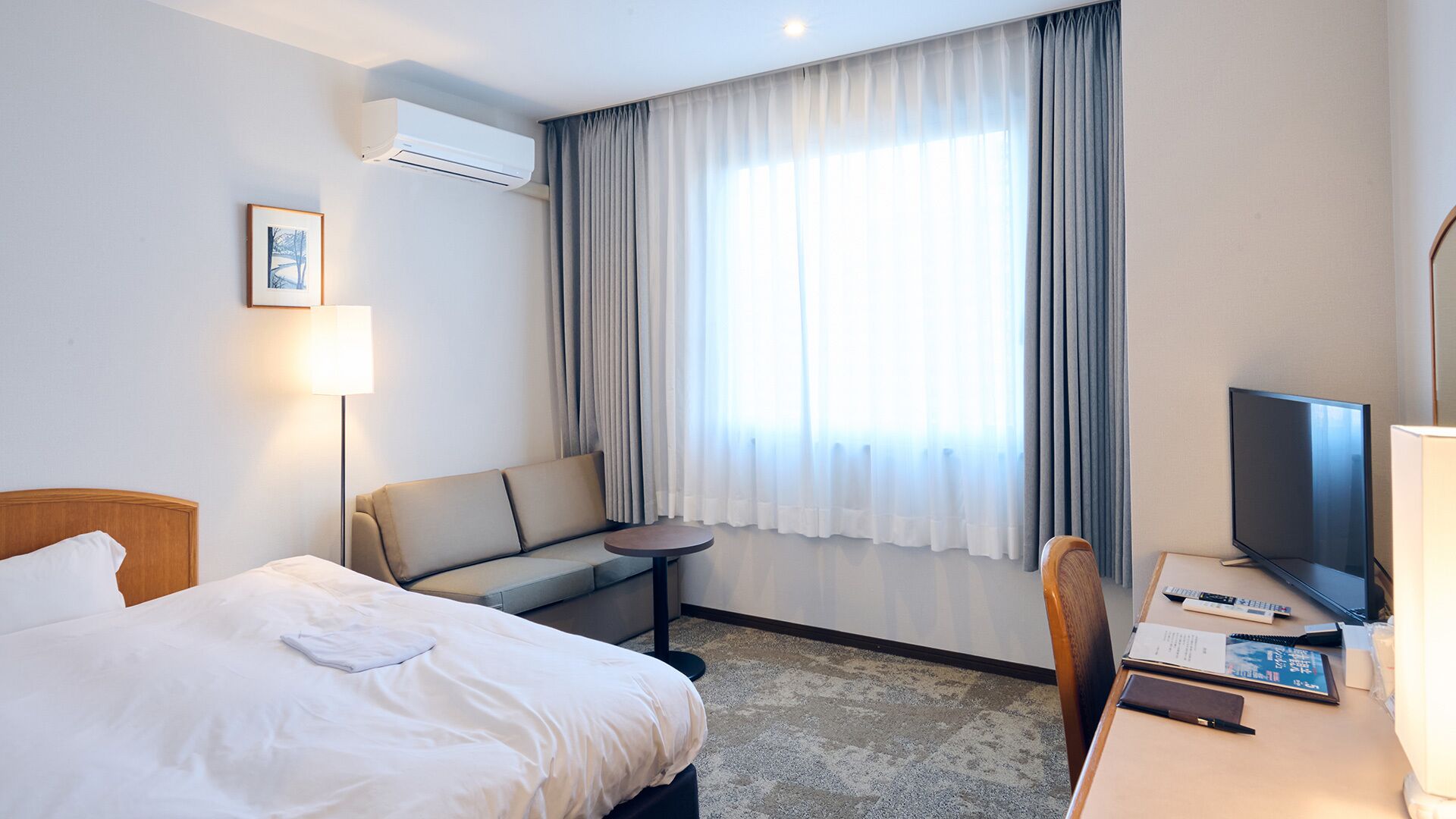 A hotel room with a bed, a sofa, a small table, a TV, and a desk with a chair.