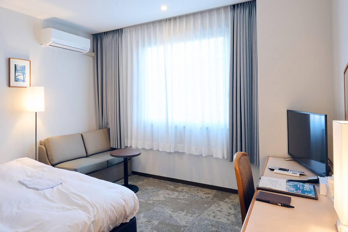 A hotel room with a bed, a sofa, a small table, a TV, and a desk with a chair.