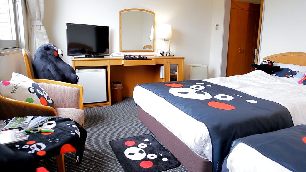 A hotel room with a bed, a desk with a computer, a chair, and a television.