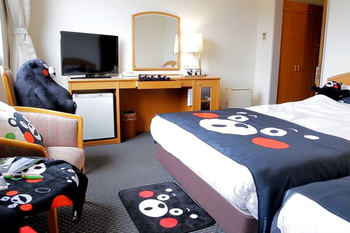 A hotel room with a bed, a desk with a computer, a chair, and a television.