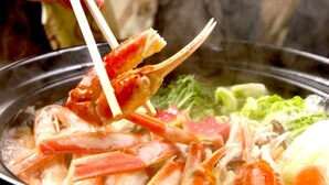 A person holding a crab with chopsticks over a pot of boiling soup with vegetables. - Minshuku Ryokan Sato no Yado Kawajiri (Miyazu)