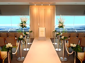 An aisle with chairs and a podium with a cross, flanked by floral arrangements. - Royal Hotel Miyakonojo (Miyakonojo)