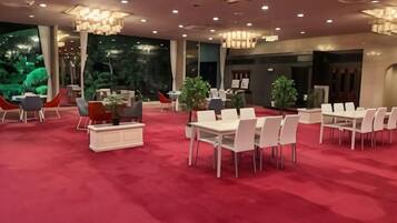 A spacious indoor area with multiple tables and chairs, a red carpet floor, and a large window with a view of greenery.