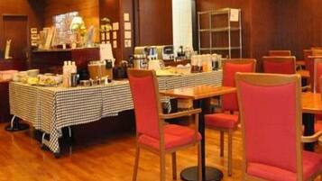 A hotel room with a wooden floor, a checkered tablecloth, red chairs, and a coffee station.