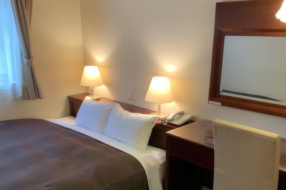 A hotel room with a bed, two bedside lamps, a desk with a telephone, and a chair.