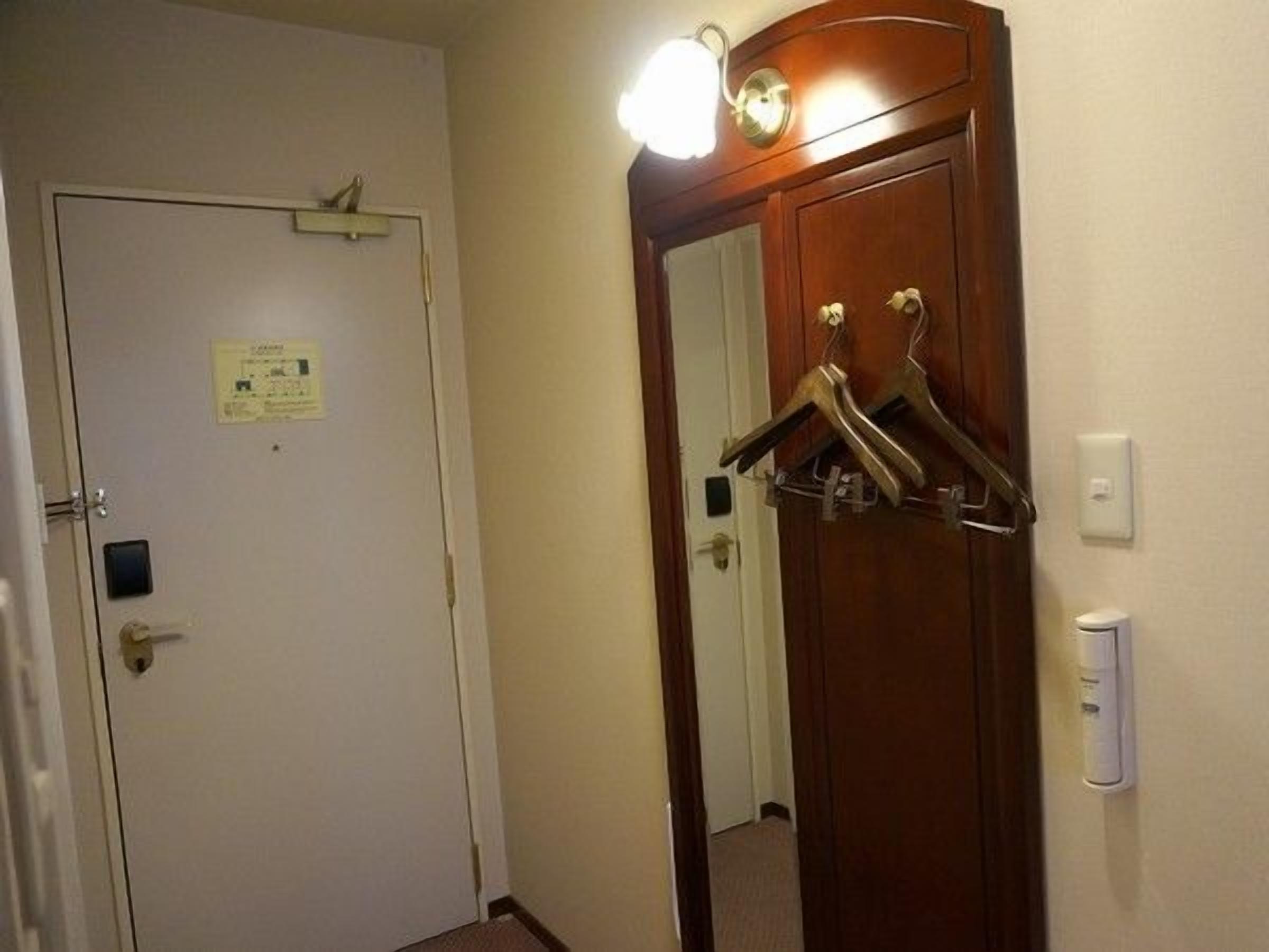 A hotel room with a white door, a coat rack with hangers, a light switch, and a wall-mounted light fixture.