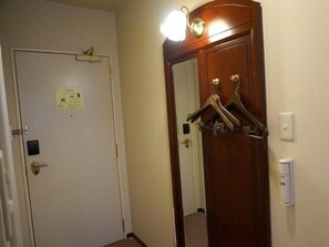 Habitación de hotel con una puerta blanca, perchero con ganchos, interruptor de luz y una lámpara fijada a la pared.