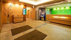 A hotel reception area with a wooden reception desk, a digital screen, and a green wall with a geometric pattern. - Super Hotel Kadoma (Kadoma)