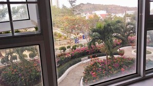 A view from a window overlooking a landscaped garden with a palm tree, benches, and a variety of flowering plants. - WELCOME TO MOONLIGHT OSC (Tp. Vũng Tàu)