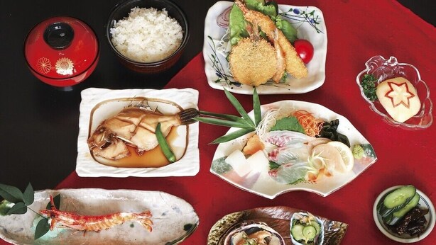 Variedad de platos japoneses sobre un mantel rojo, incluyendo sushi, arroz y mariscos.