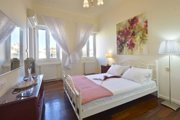 A bedroom with a bed, a bedside table, a lamp, a window with curtains, and a painting on the wall.