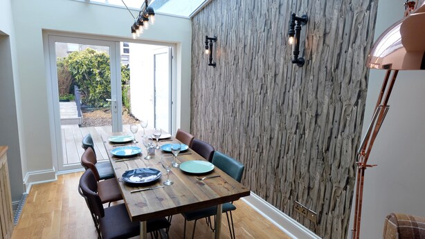 Un coin repas avec une table en bois dressée pour quatre personnes, entourée de chaises, et une vue sur le jardin à travers des portes vitrées.