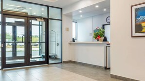 A modern reception area with glass doors leading to a parking area, a clock on the wall, and a framed painting.