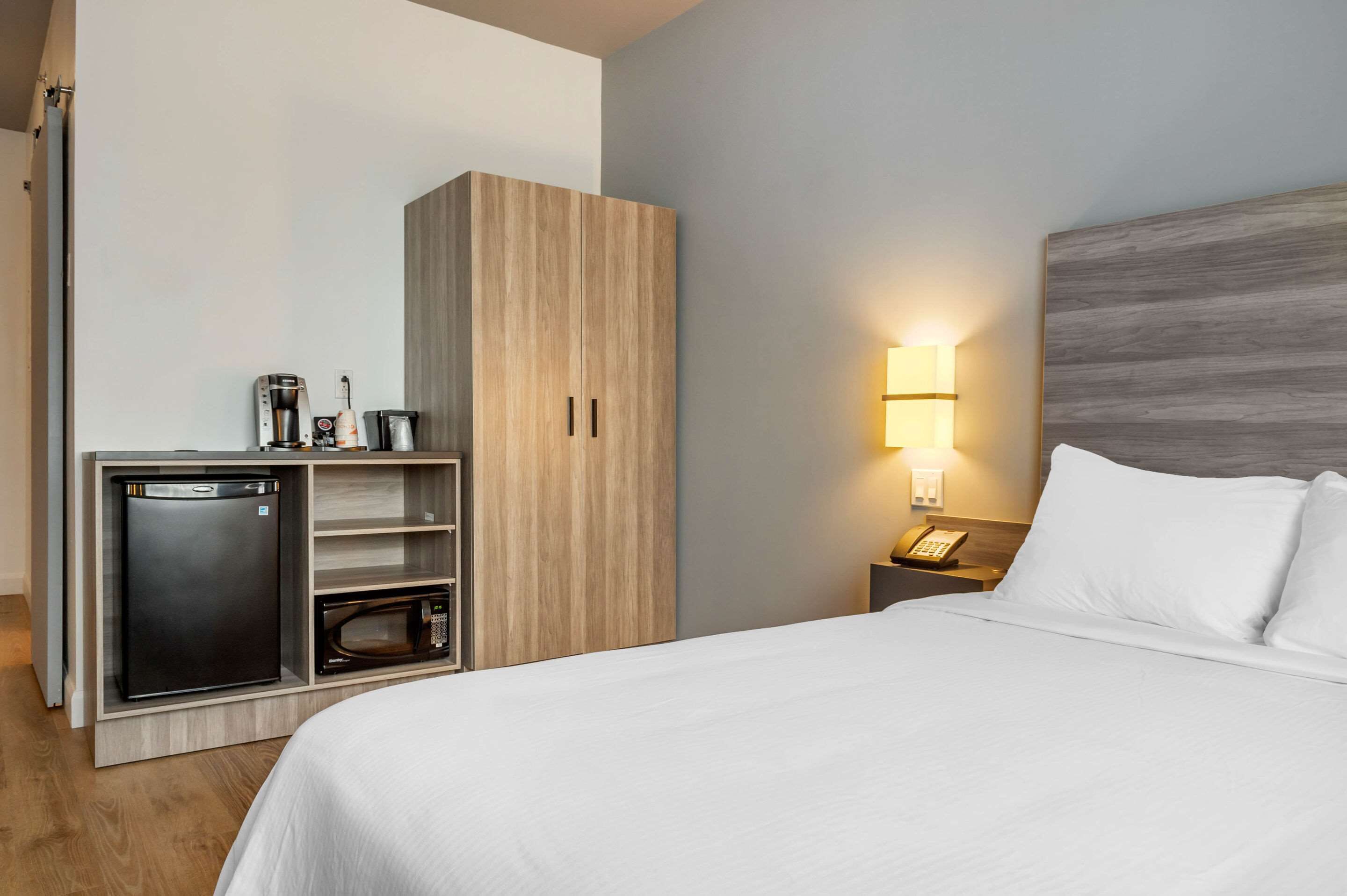 A hotel room with a bed, a wardrobe, a minibar, a lamp, and a telephone.