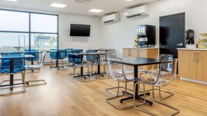 A modern conference room with glass tables and chairs, a large window with a view, and a coffee machine.