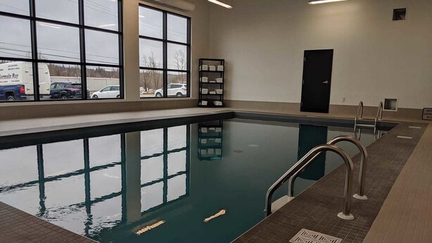 An indoor swimming pool with clear glass walls, a tiled floor, and metal handrails.