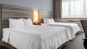 A hotel room with two beds, a nightstand with a phone, a lamp, and a window with curtains.