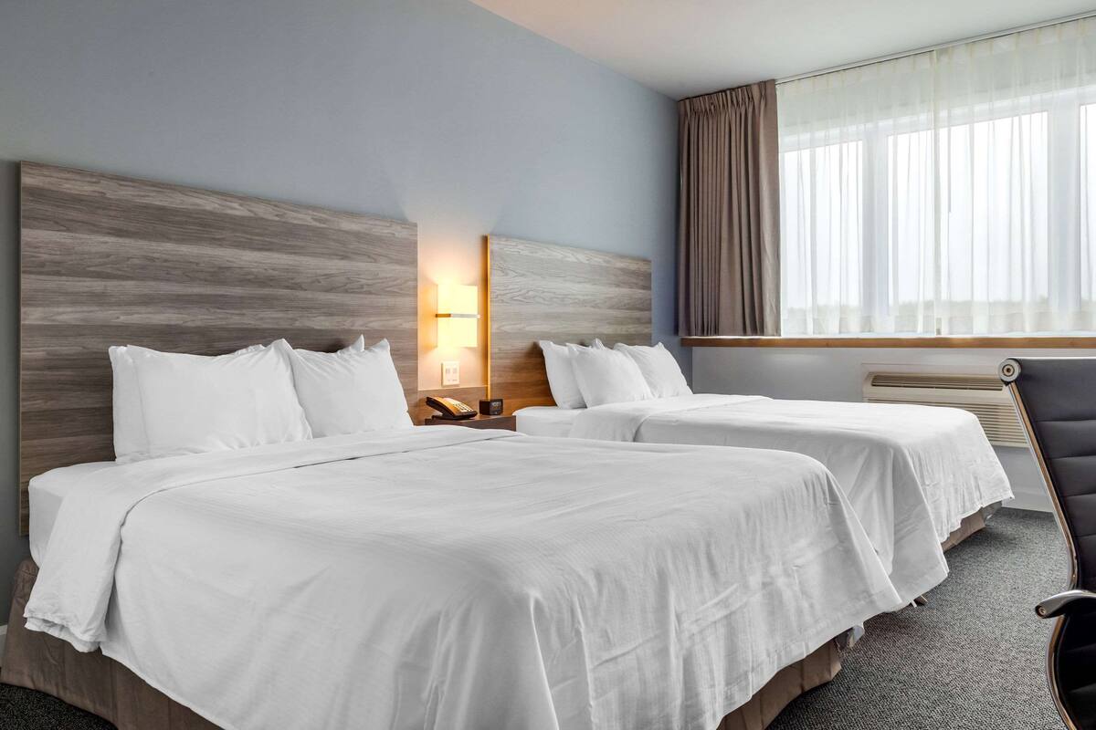 A hotel room with two beds, a nightstand with a phone, a lamp, and a window with curtains.