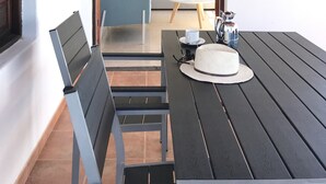 An outdoor dining area with a table and chairs, a lamp, and a painting on the wall.