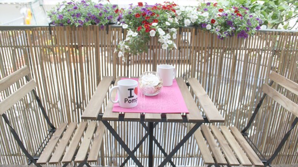 Una mesa de madera con un posavasos rosa, dos tazas blancas y un vaso con tapa rosa.