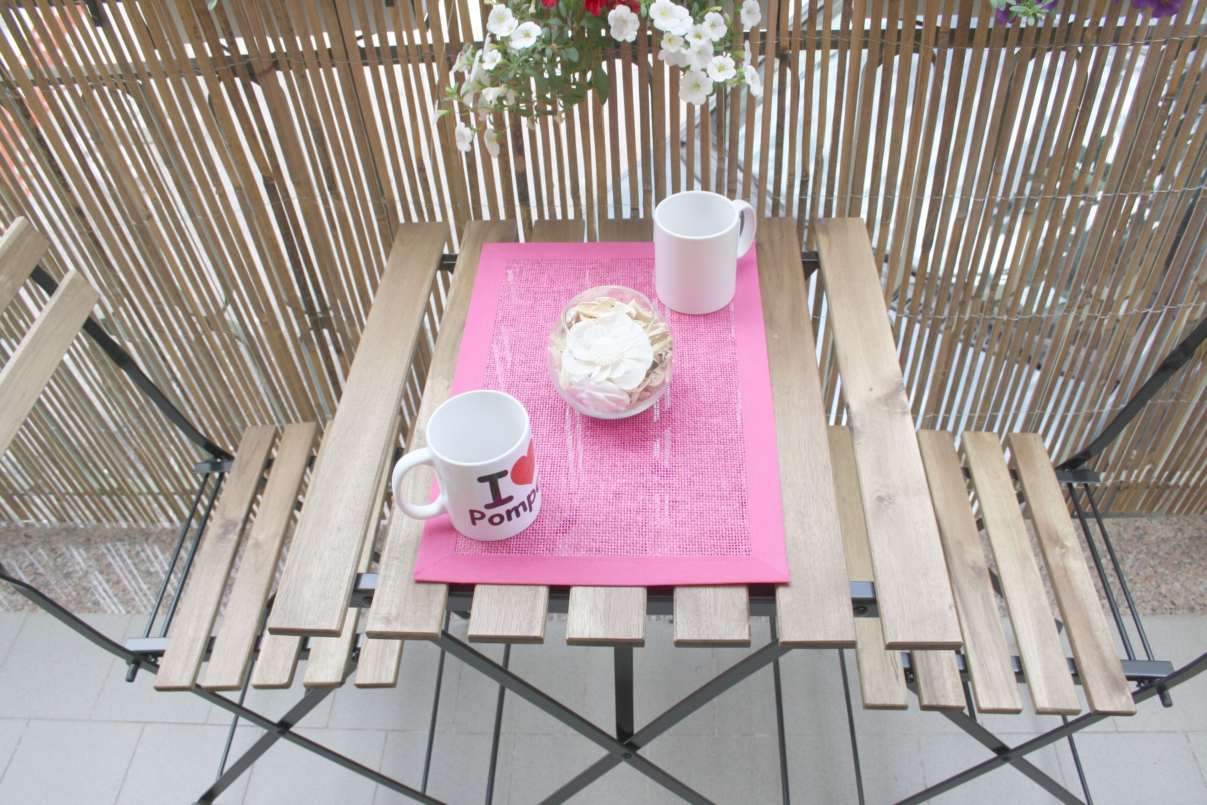 Una mesa de madera con un posavasos rosa, una taza blanca y un postre.