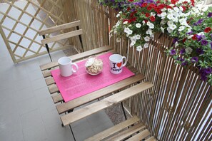 Un banc en bois sur lequel sont posés un set de table rose, deux tasses blanches et un bol rempli de fleurs séchées.