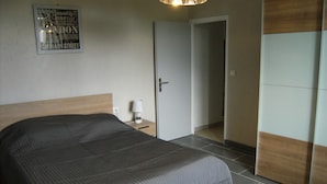Et soveværelse med seng, et natbord, en lampe og en dør til et andet rum.