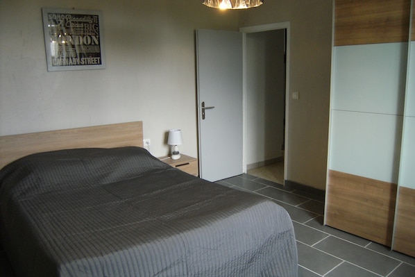 A bedroom with a bed, a nightstand, a lamp, and a door leading to another room. - house in a village of the enclave of the popes (Grillon)