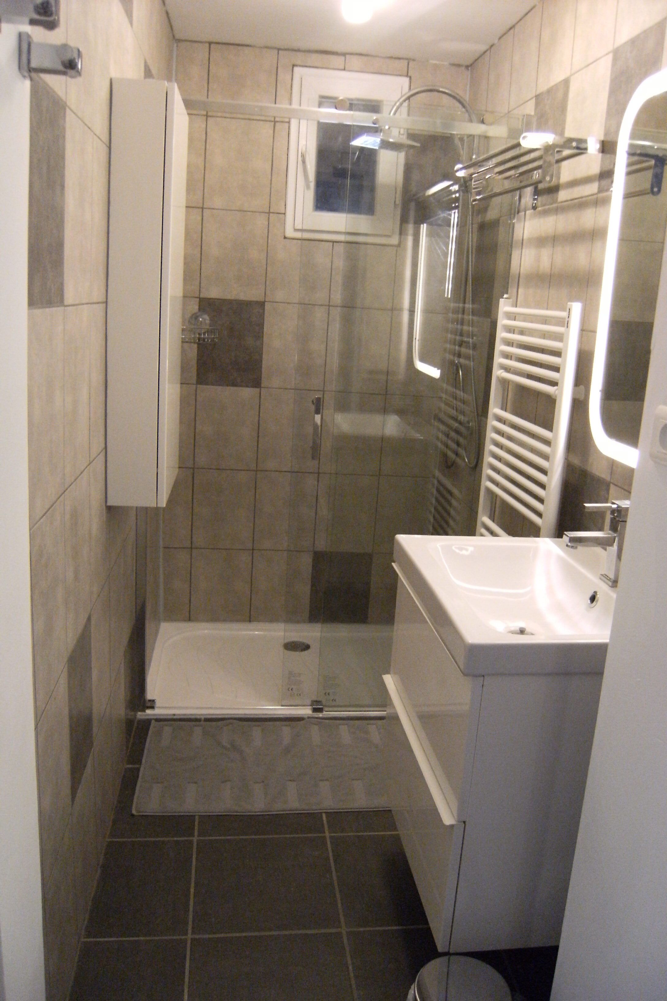 Een kleine badkamer met een douche, wastafel en spiegel.