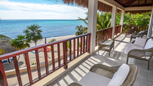 Un balcón con mobiliario de mimbre, vista a la playa y palmeras.
