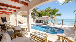 Zona junto a la piscina con sillones, una mesa de cristal y vista al océano.