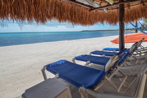 A beach with lounge chairs and a thatched roof structure.