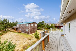 Overlooking a serene grassy area, this property features a spacious deck with a railing and a two-story building in the background.