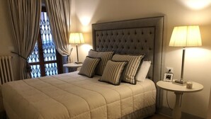 A neatly made bed with a tufted headboard, two bedside tables with lamps, and a window with curtains. - Luxury in the Piazza in Greve In Chiant (Greve in Chianti)