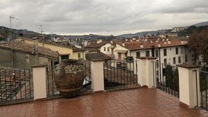 A rooftop terrace with a large terracotta pot, a metal gate, and a view of a town with terracotta-roofed buildings. - Luxury in the Piazza in Greve In Chiant (Greve in Chianti)