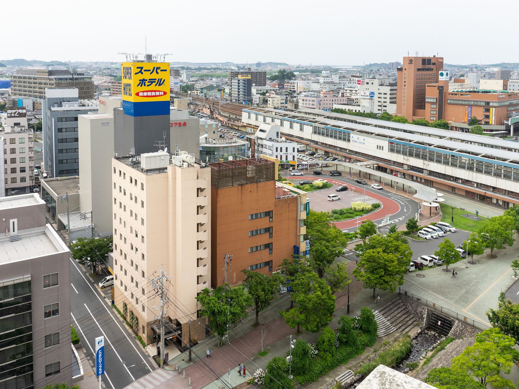 Un hotel di grandi dimensioni con un cartello ben visibile, circondato da edifici urbani e una linea tramviaria.