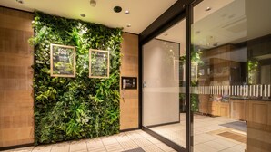 A reception area with a green wall, framed posters, a phone, and a glass door leading to a lobby. - Super Hotel Tottori Ekimae (Tottori)