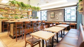 A modern restaurant with wooden tables and chairs, a long counter, and a brick wall with greenery. - Super Hotel Tottori Ekimae (Tottori)