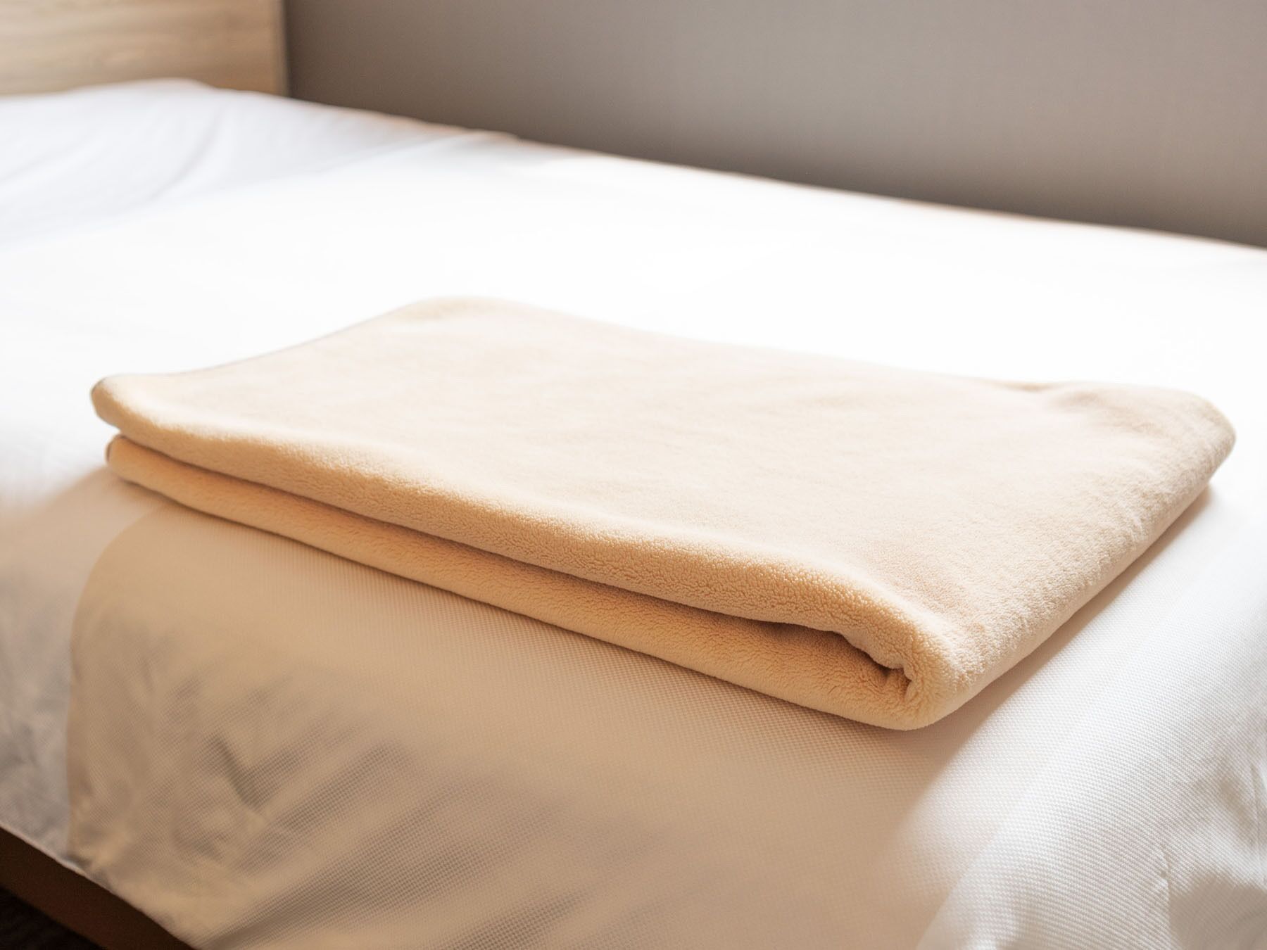Una cama bien hecha con una manta beige doblada.