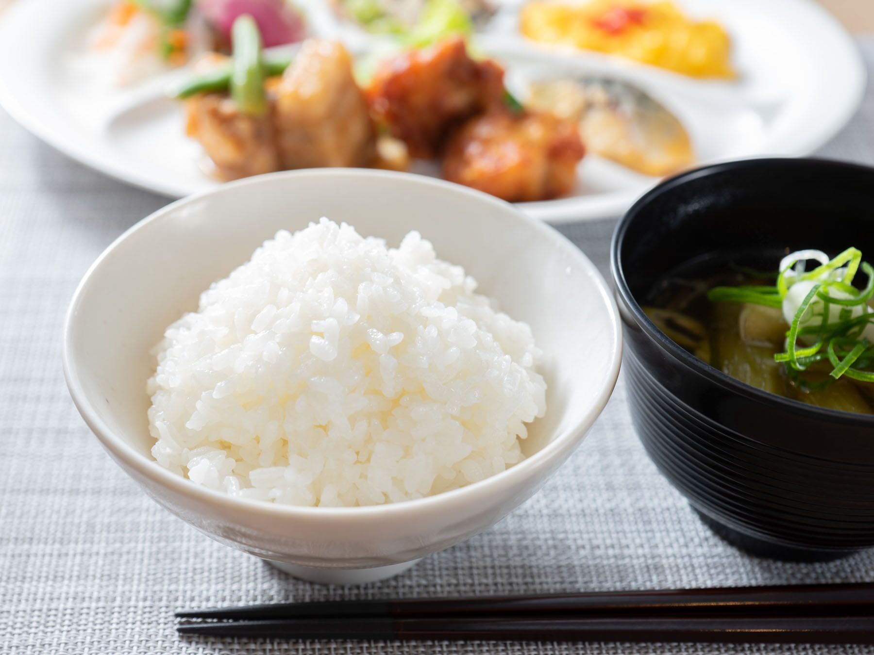 Un bol de riz blanc, un bol de soupe aux oignons verts et une assiette avec divers plats en arrière-plan.