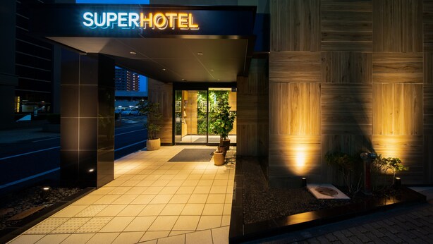The entrance to a hotel with a neon sign, a tiled pathway, and a wooden wall. - Super Hotel Tottori Ekimae (Tottori)