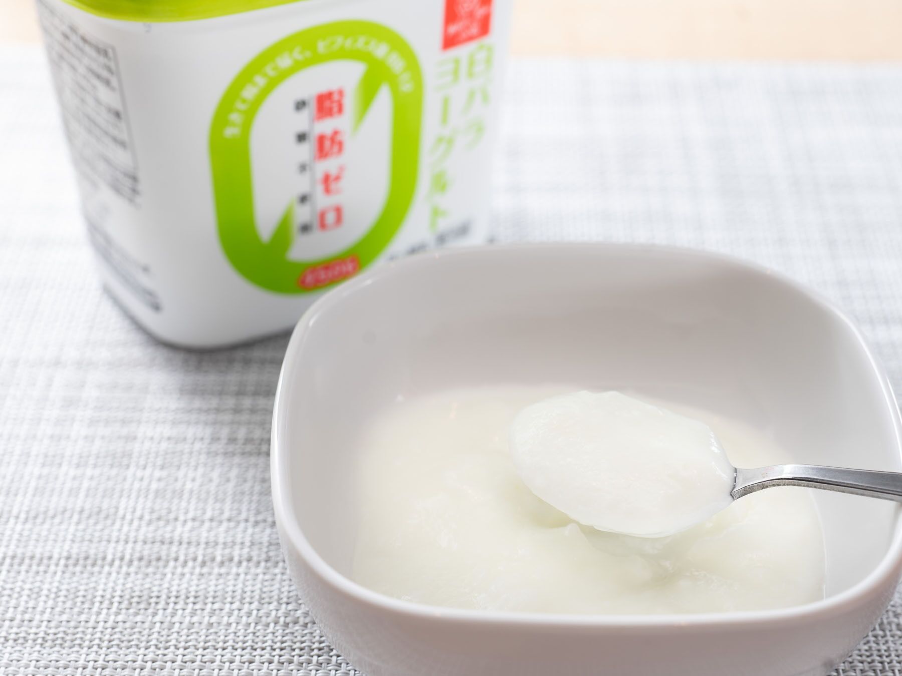 A bowl of white liquid with a spoon, placed on a textured surface.