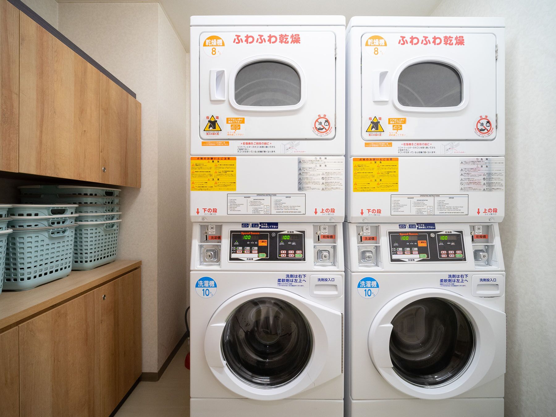 Two front-loading washing machines with control panels, safety instructions, and a wooden cabinet with laundry baskets.