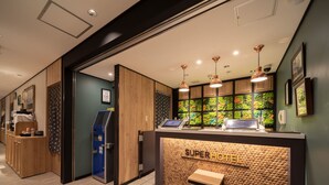 A hotel reception area with a wooden reception desk, a self-service kiosk, and a green wall with a vertical garden. - Super Hotel Tottori Ekimae (Tottori)