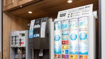 A coffee machine and a water dispenser with various drink options and a sign indicating free beverages for breakfast hours.