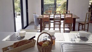 Un coin repas avec une table dressée pour quatre personnes, comprenant des chaises, un panier de pain et un saladier de fruits.