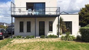 Une maison moderne à deux étages, dotée d’un balcon, avec une voiture garée dans l’allée et une pelouse bien entretenue.