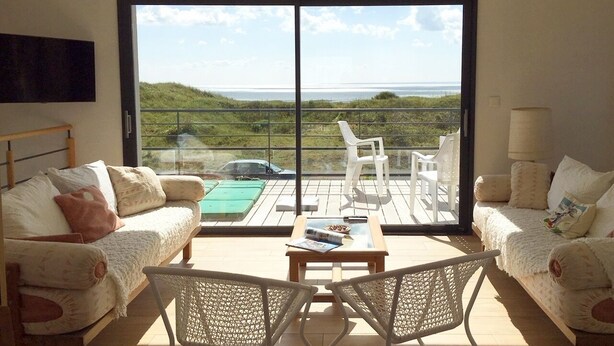 Un salon spacieux doté d’une grande porte-fenêtre coulissante donnant sur un balcon avec vue sur la mer.