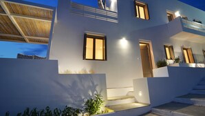 Una casa moderna de dos pisos con techo plano, ventanas amplias y una escalera que lleva al nivel superior.